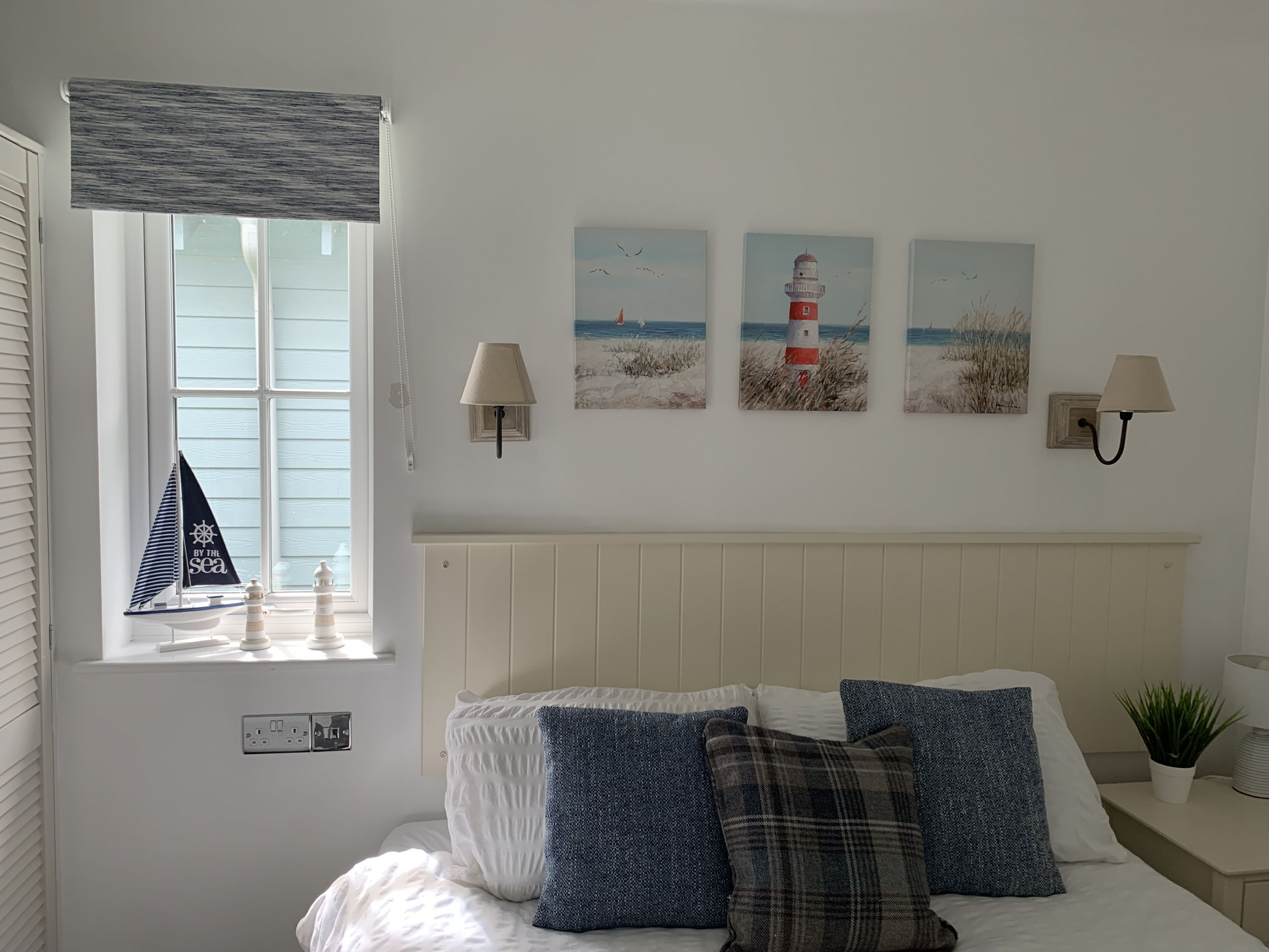 Een slaapkamer met een bed, een raam met uitzicht op zee en drie schilderijen aan de muur.