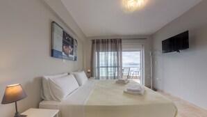 Een hotelkamer met een bed, een televisie, een lamp, een raam met gordijnen en uitzicht op zee.