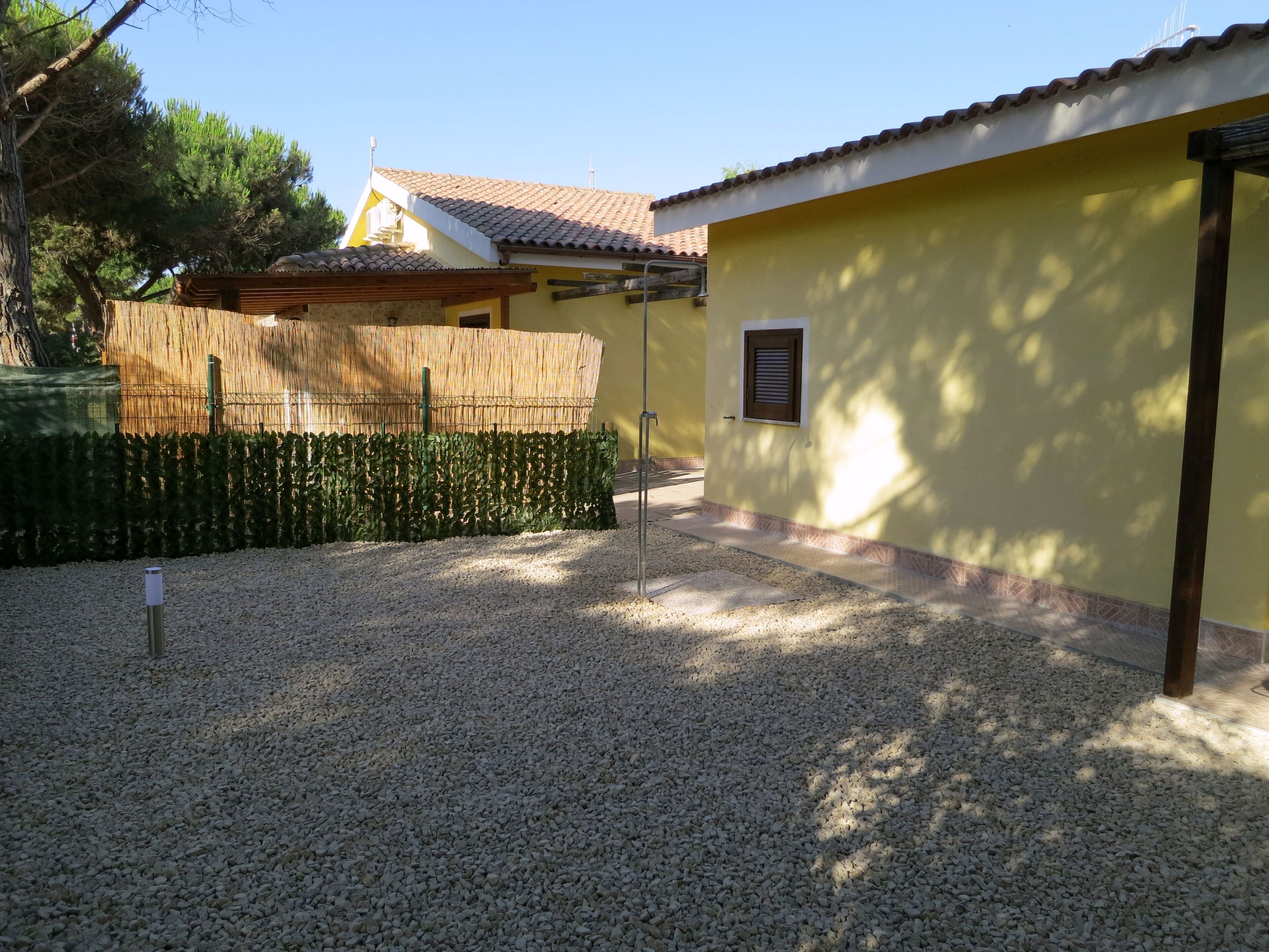 A yellow building with a tiled roof, a gravel driveway, and a bamboo fence.