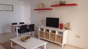 A modern living room with a white TV stand, red chairs, a dining table with chairs, and a red sofa. - Spacious, large terrace, sunny, WiFi, from the sea, 250 m. from the beach (Morro Jable)