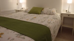 A neatly made bed with floral bedding and a green throw, flanked by bedside tables with lamps. - Spacious, large terrace, sunny, WiFi, from the sea, 250 m. from the beach (Morro Jable)