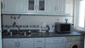 A kitchen with white cabinets, a double sink, a coffee maker, a microwave, and a washing machine.