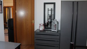 A room with a wooden door, a dresser with drawers, a mirror, and a refrigerator.