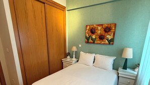A bedroom with a large bed, wooden wardrobe, two bedside tables with lamps, and a floral painting on the wall.