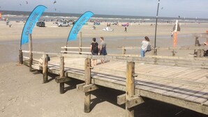 A wooden pier with blue banners, leading to a sandy beach with people and kites. - Charming, spacious town house, Friedrichstadt n. North Sea / 2-4 pers (Friedrichstadt)