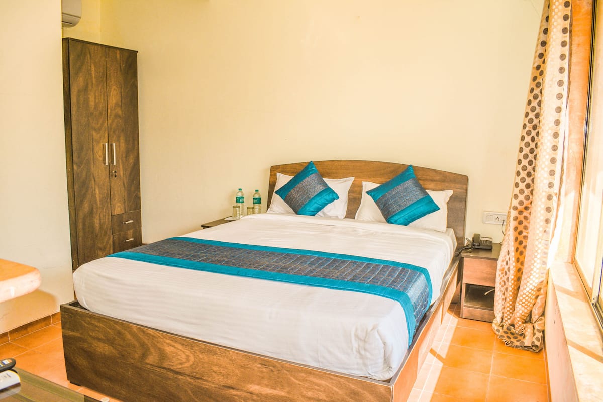 Uma cama bem arrumada com cabeceira de madeira, mesa de cabeceira com telefone e cortina estampada com bolinhas.