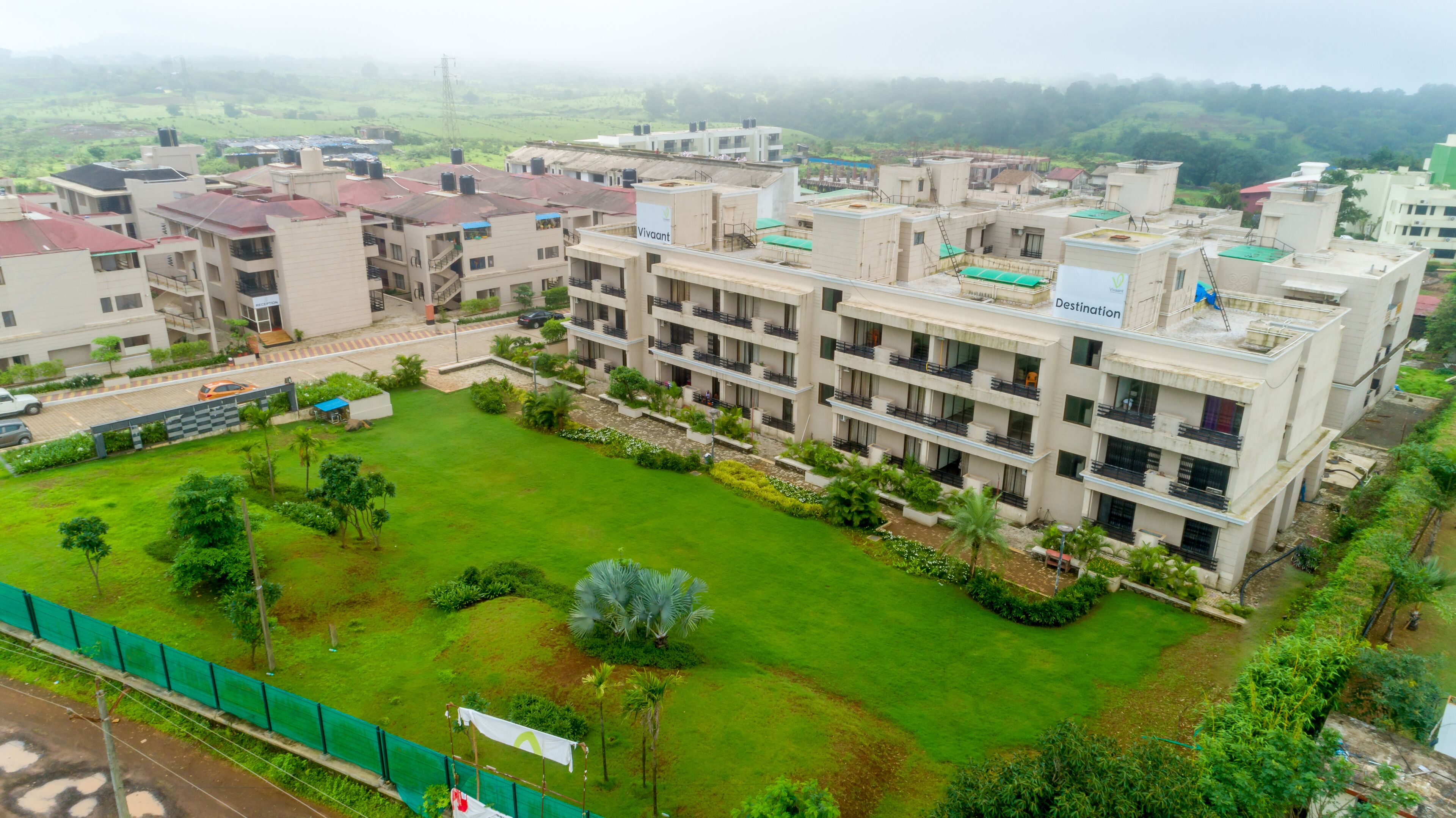 A multi-story hotel with a central courtyard, surrounded by greenery and a view of the countryside.