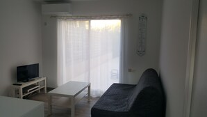 A living room with a sofa, a TV on a stand, a table, and a window with sheer curtains. - Quiet studio near Aubagne (La Penne-sur-Huveaune)