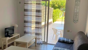 A modern living room with a sofa, a TV, a table, and a sliding glass door leading to an outdoor patio. - Quiet studio near Aubagne (La Penne-sur-Huveaune)