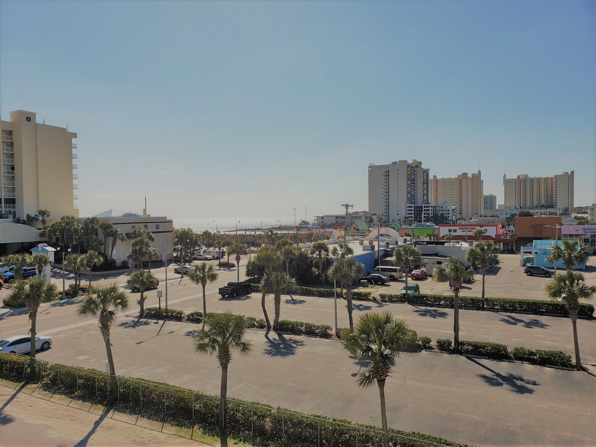 Ein Parkplatz mit Palmen, einem Hotel und einem Strand im Hintergrund.