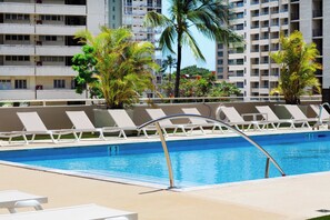 Una piscina con sillas de descanso y palmeras, rodeada de edificios altos.