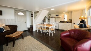 A spacious living area with a dining table, a red leather sofa, and a staircase leading to a kitchen.