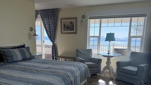 A bedroom with a bed, two striped armchairs, a small table with a lamp, a patterned rug, and a large window with a view of the sea. - The Lookout Lodge on Bishop's Beach with Spectacular views of Kachemak Bay! (Homer)