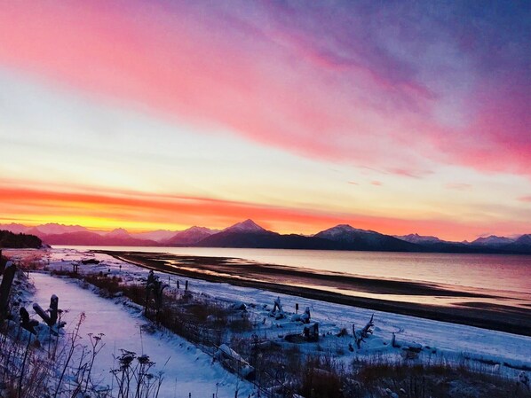 Paesaggio innevato con specchio d'acqua e montagne sullo sfondo.