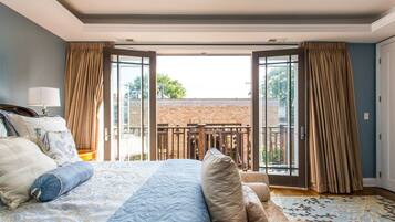 Une chambre à coucher avec un grand lit, un canapé et une vue sur un bâtiment en briques, visible à travers de grandes portes-fenêtres ouvertes.