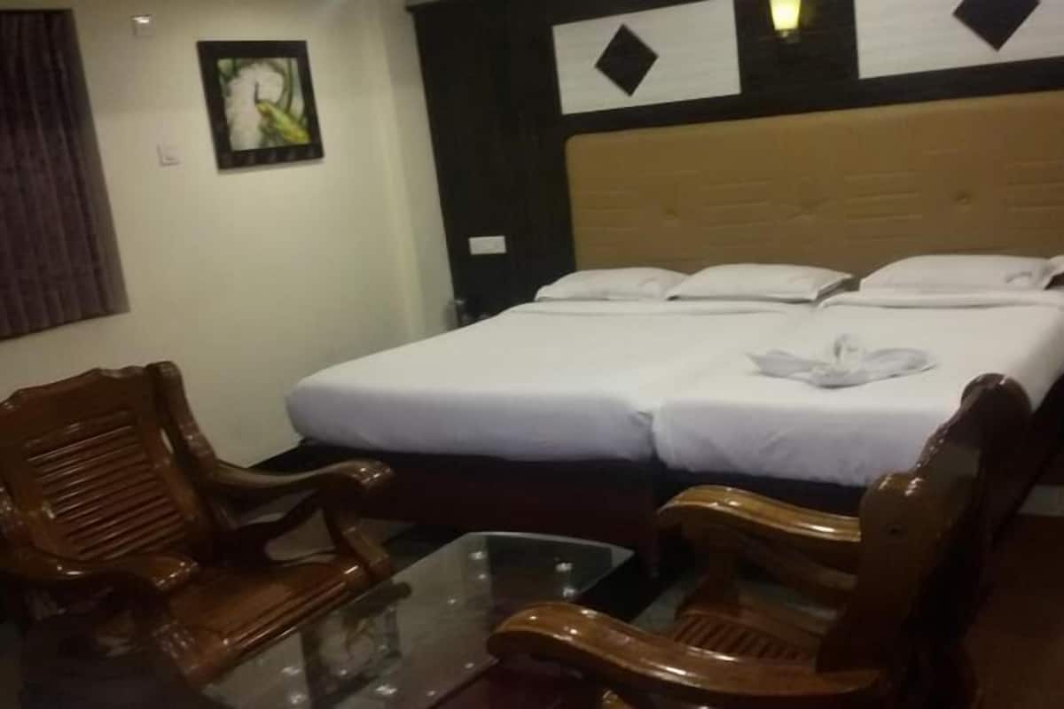 A hotel room with a double bed, two wooden chairs, a small table, and a wall with framed pictures.