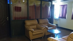 A room with a leather armchair, a small round table, and a window with curtains. - Hotel Aakash Residency (Madurai)