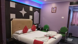 A hotel room with a bed, two green chairs, a nightstand, and a star decoration on the headboard. - Hotel Aakash Residency (Madurai)
