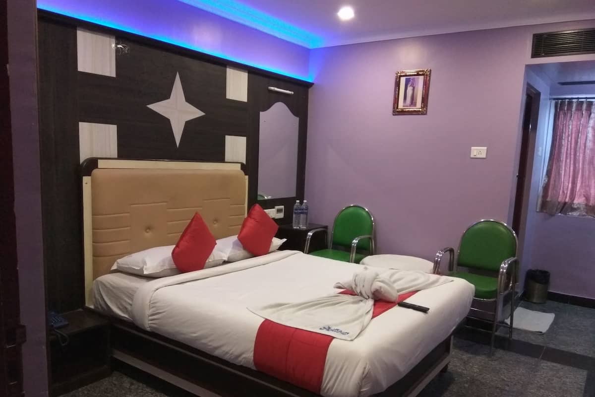 A hotel room with a bed, two green chairs, a nightstand, and a star decoration on the headboard.
