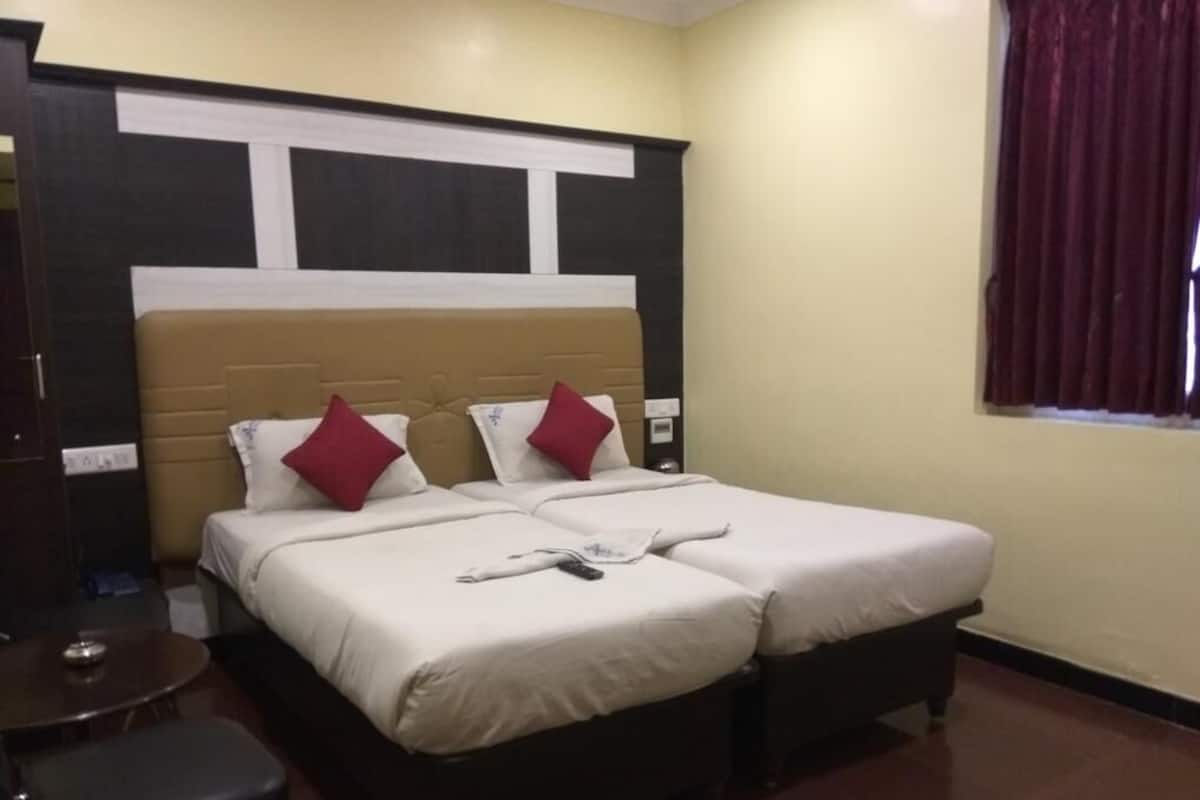 A hotel room with a double bed, two pillows, a bedside table, and a window with curtains.