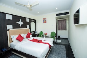 A hotel room with a bed, a desk, two chairs, a ceiling fan, and a TV.