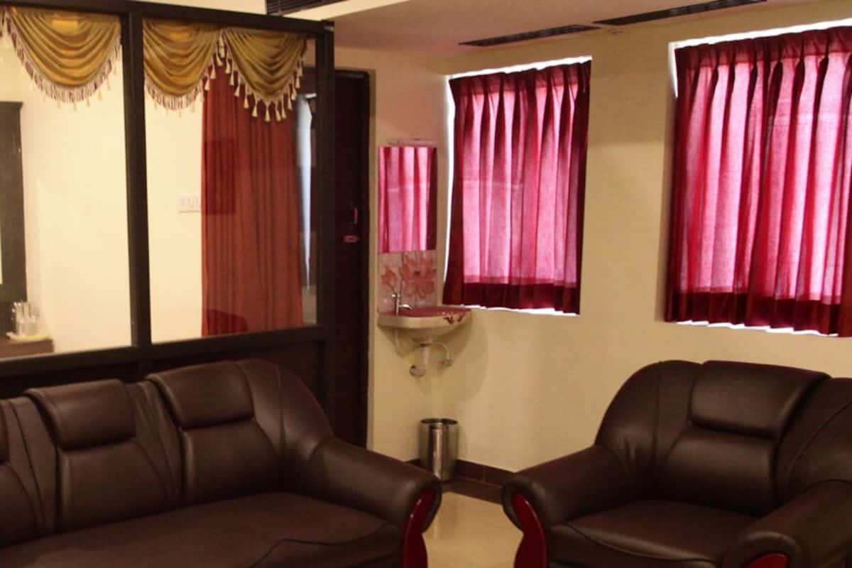 A living room with a brown leather sofa, two armchairs, a wooden cabinet, and a large window with curtains.