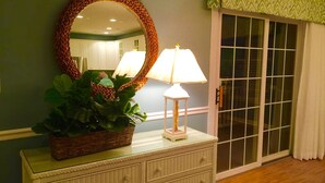 A room with a wicker dresser, a mirror, a lamp, and a sliding glass door. - EXTREME OCEANFRONT -  Heated Pool & Hot Tub / Linens & Gas grill inc. discounted (Surfside Beach)
