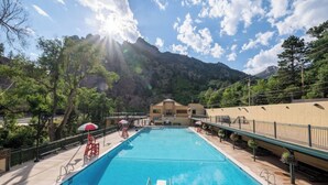 Une piscine avec vue sur les montagnes, entourée d’arbres et donnant sur un bâtiment doté d’un balcon.