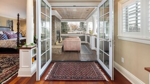 Une chambre avec un grand lit, une table de chevet et une commode. Il y a une fenêtre avec des volets blancs et une vue sur les arbres à l’extérieur.