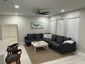 Un salon moderne avec un canapé d’angle, une table basse et un ventilateur de plafond.