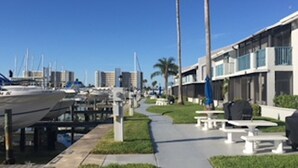 A marina with boats docked, a pathway, and modern buildings with outdoor seating. - Bayside Condo with Brand New Interior, Walkable to BEACH, Retail, Dining & more! (Madeira Beach)
