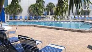 A pool area with blue lounge chairs and palm trees. - Bayside Condo with Brand New Interior, Walkable to BEACH, Retail, Dining & more! (Madeira Beach)