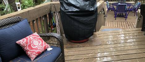 En træterrasse med grill under tag, en fletsofa med røde puder og et bord med stole.