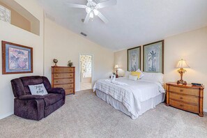 A bedroom with a bed, a chair, a nightstand, and wall art.