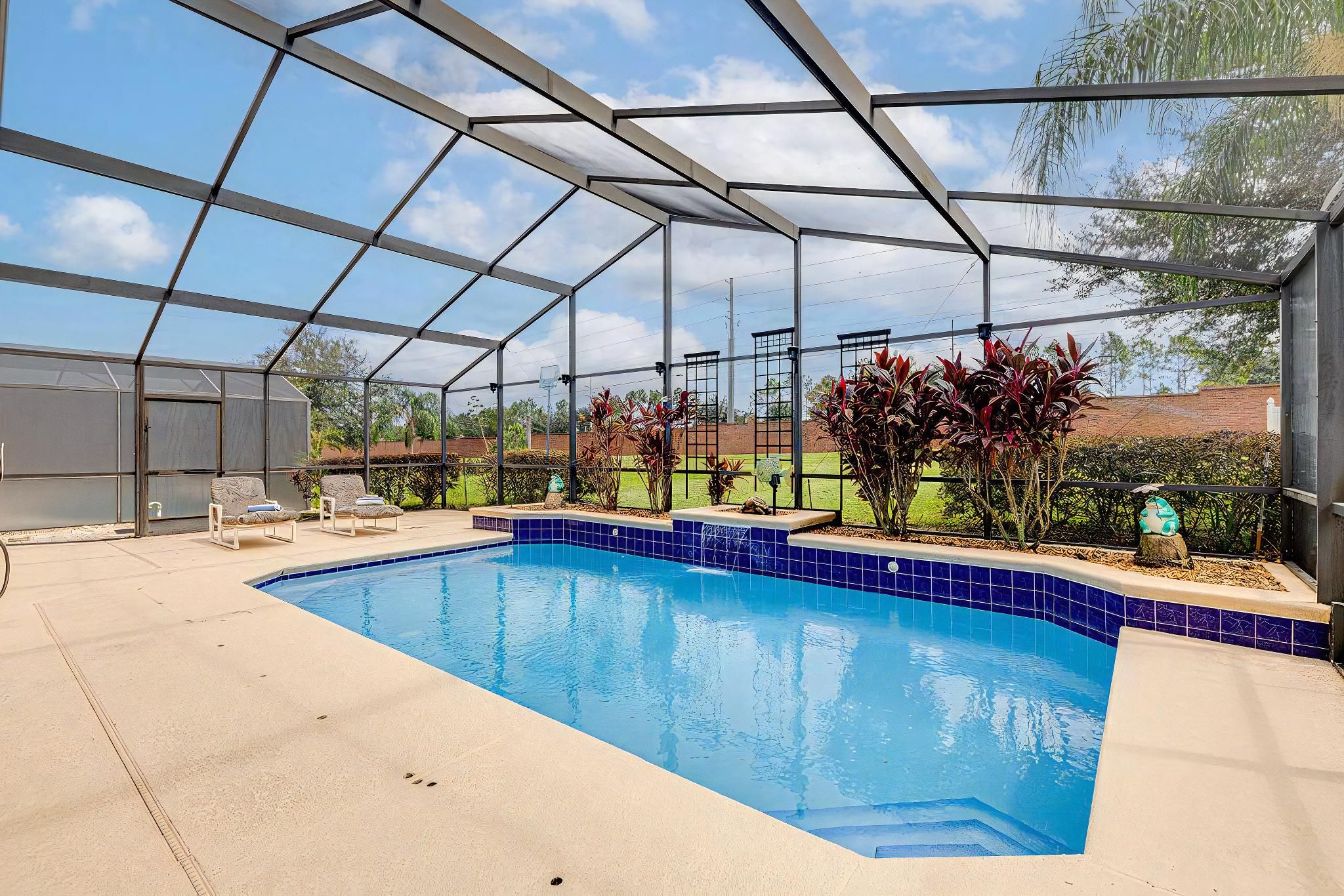Ein überdachter Swimmingpool mit blau gefliestem Rand, umgeben von einer Metallkonstruktion und Blick ins Freie.