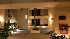 A hotel lobby with a central staircase, potted plants, and a red-framed window. - Executive 2 bed, 2 bath, Penthouse, Paradise Village, el Tigre, Isla Palmares (Nuevo Vallarta)