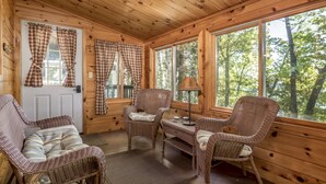 A cozy cabin interior with wooden walls, large windows, wicker furniture, and plaid curtains. - Perfect Cabin on Lake Minocqua! (Minocqua)