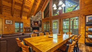 L’intérieur d’un chalet en bois comprend une grande table à manger, des murs en bois, une cheminée en pierre et un banc en cuir.