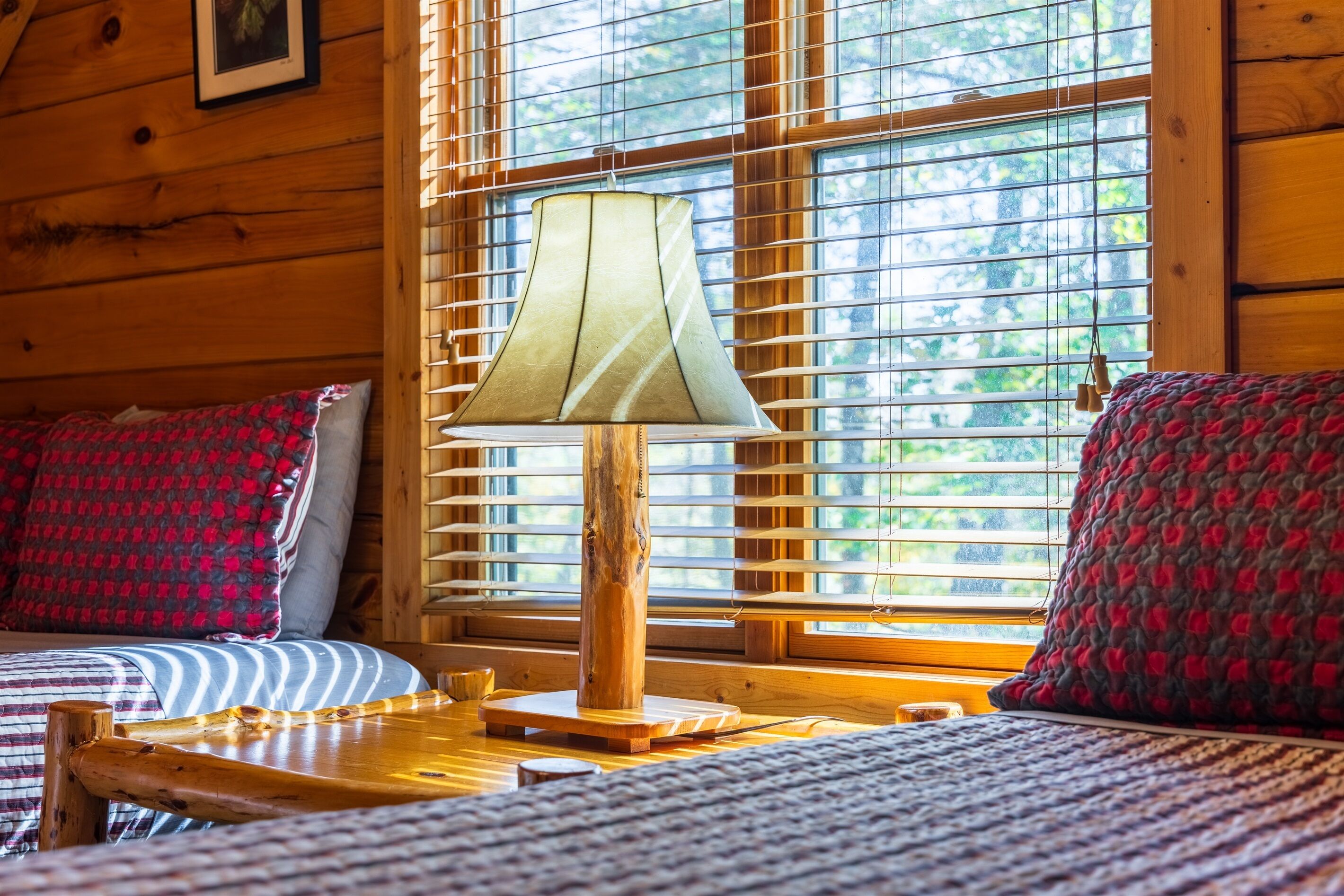 A wooden cabin room with a bed, a table, and a lamp.