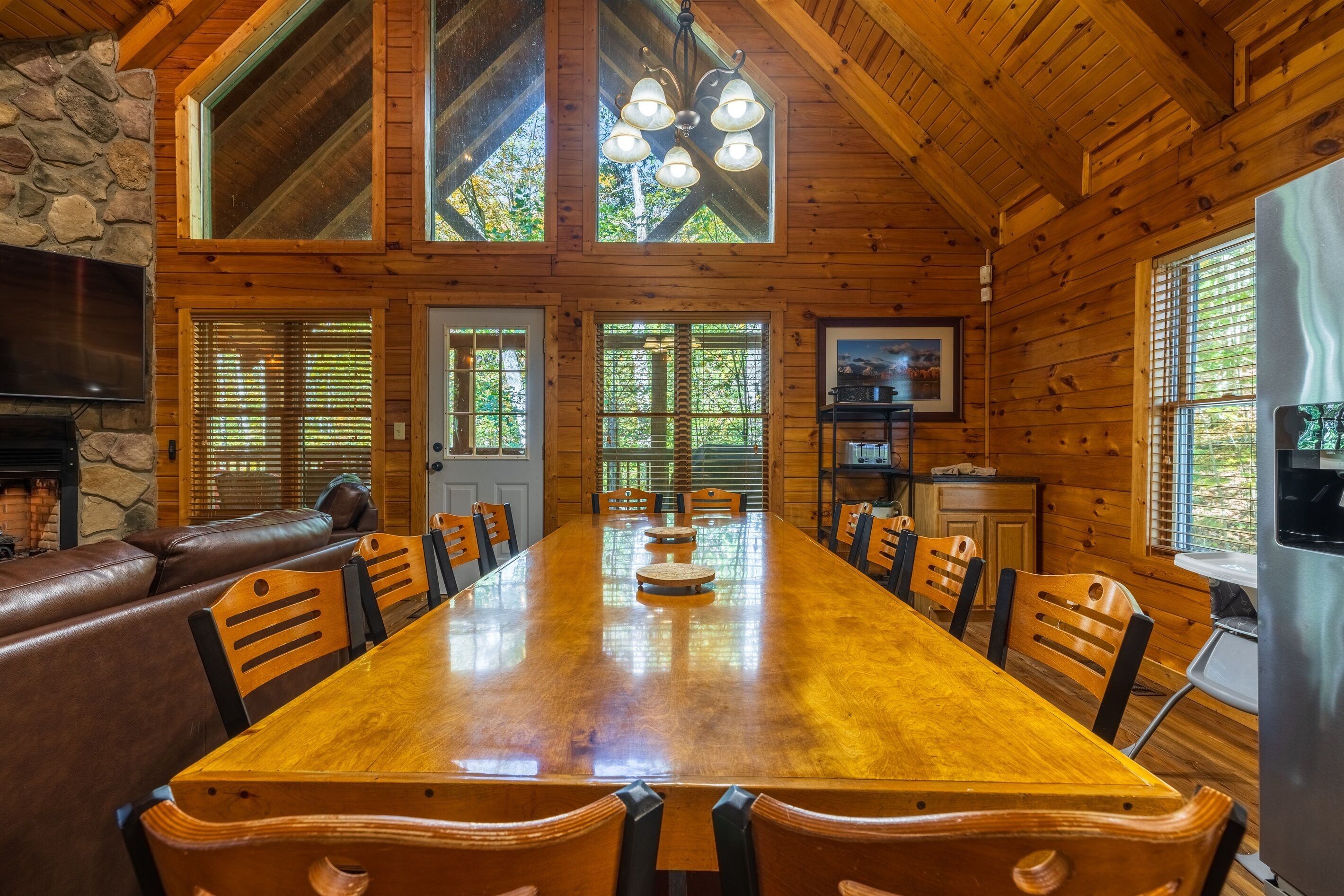 A wooden dining room with a long table, chairs, a fireplace, and large windows.