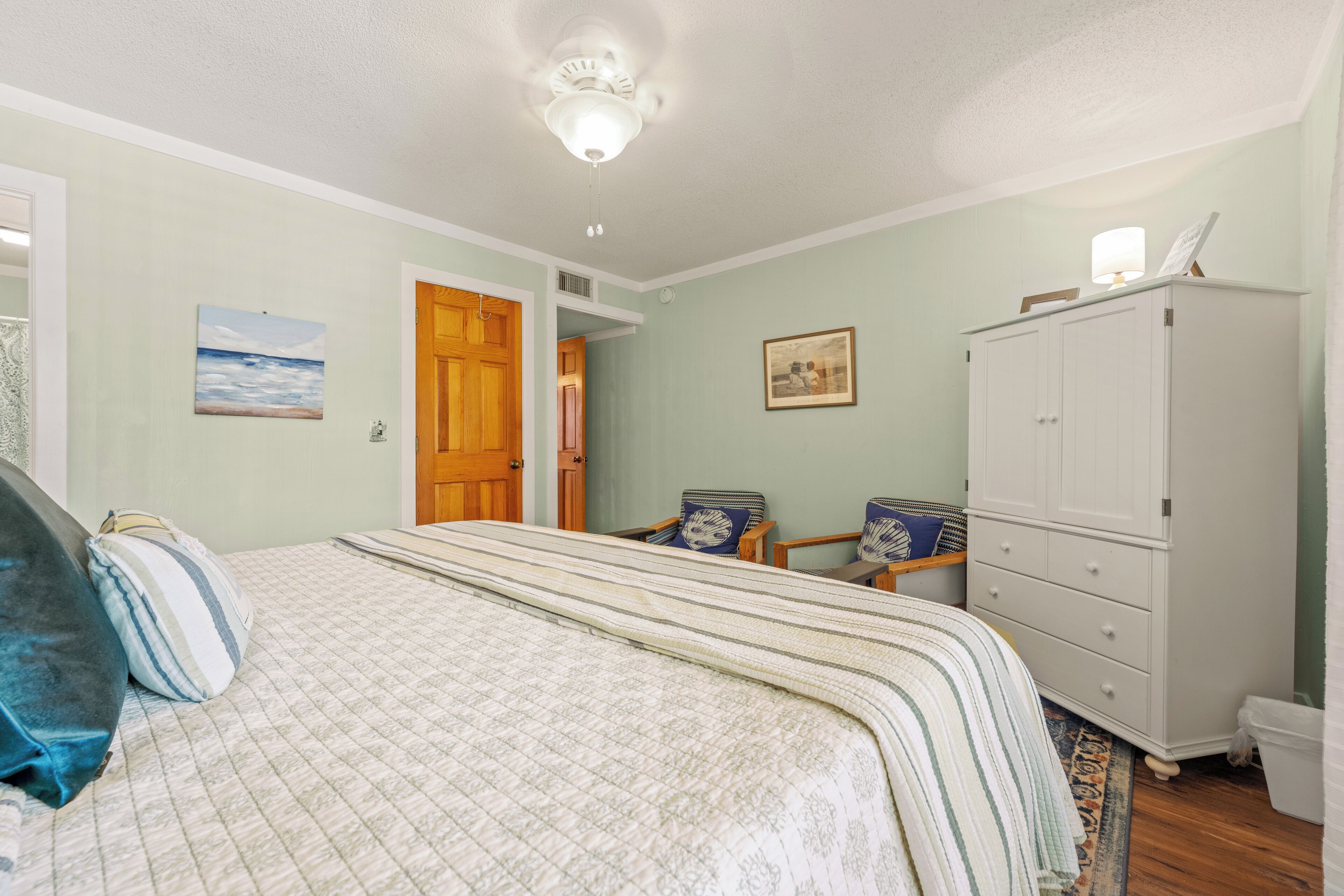 Un dormitorio con cama, armario, silla y puerta que da a otra habitación.