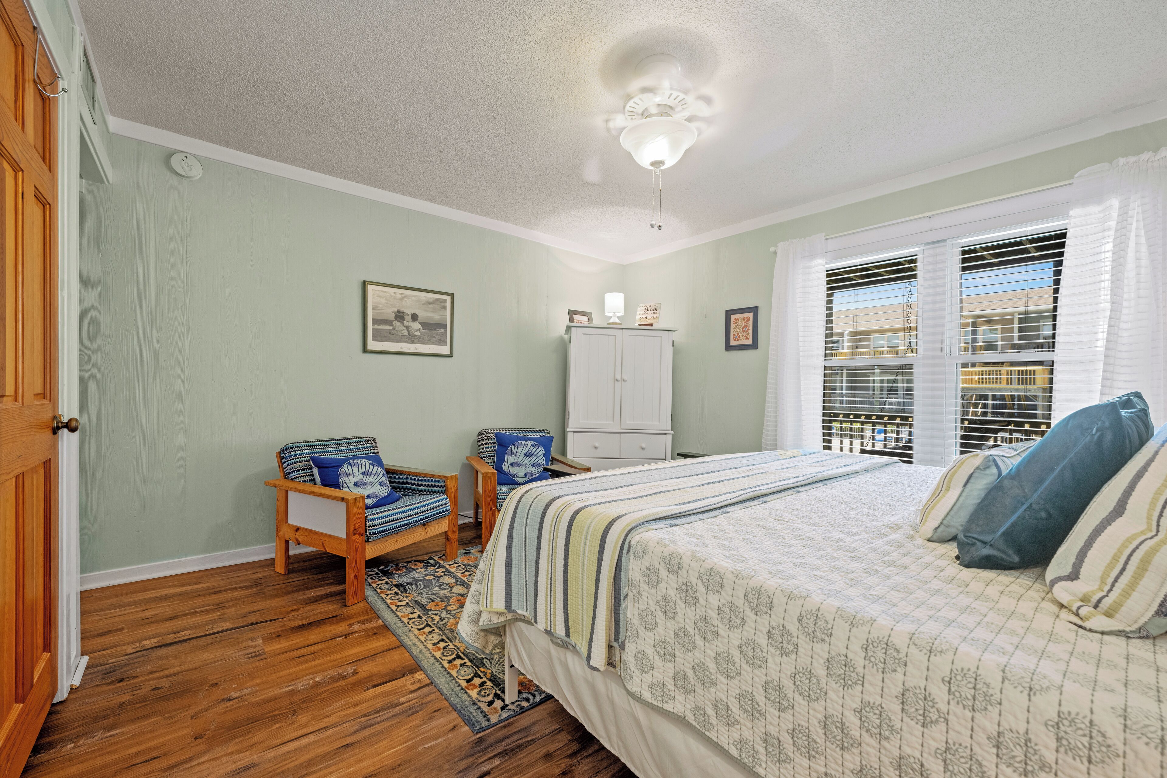 A bedroom with a bed, a chair, a wardrobe, and a window with blinds.