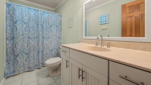 A bathroom with a patterned shower curtain, a toilet, a sink with a mirror, and cabinets. - Corolla Condo: 350 Ft to Beach, Community Pool Access at Indian Summer Condos (Corolla)