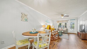A dining area with a wooden table and white chairs, a ceiling fan, and a view of the outside through a door. - Corolla Condo: 350 Ft to Beach, Community Pool Access at Indian Summer Condos (Corolla)