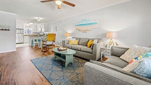A spacious living room with a ceiling fan, a grey sofa, a coffee table, and a blue patterned rug. - Corolla Condo: 350 Ft to Beach, Community Pool Access at Indian Summer Condos (Corolla)
