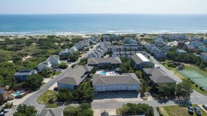 A coastal residential area with multiple two-story houses, a central swimming pool, and a beach in the background.
