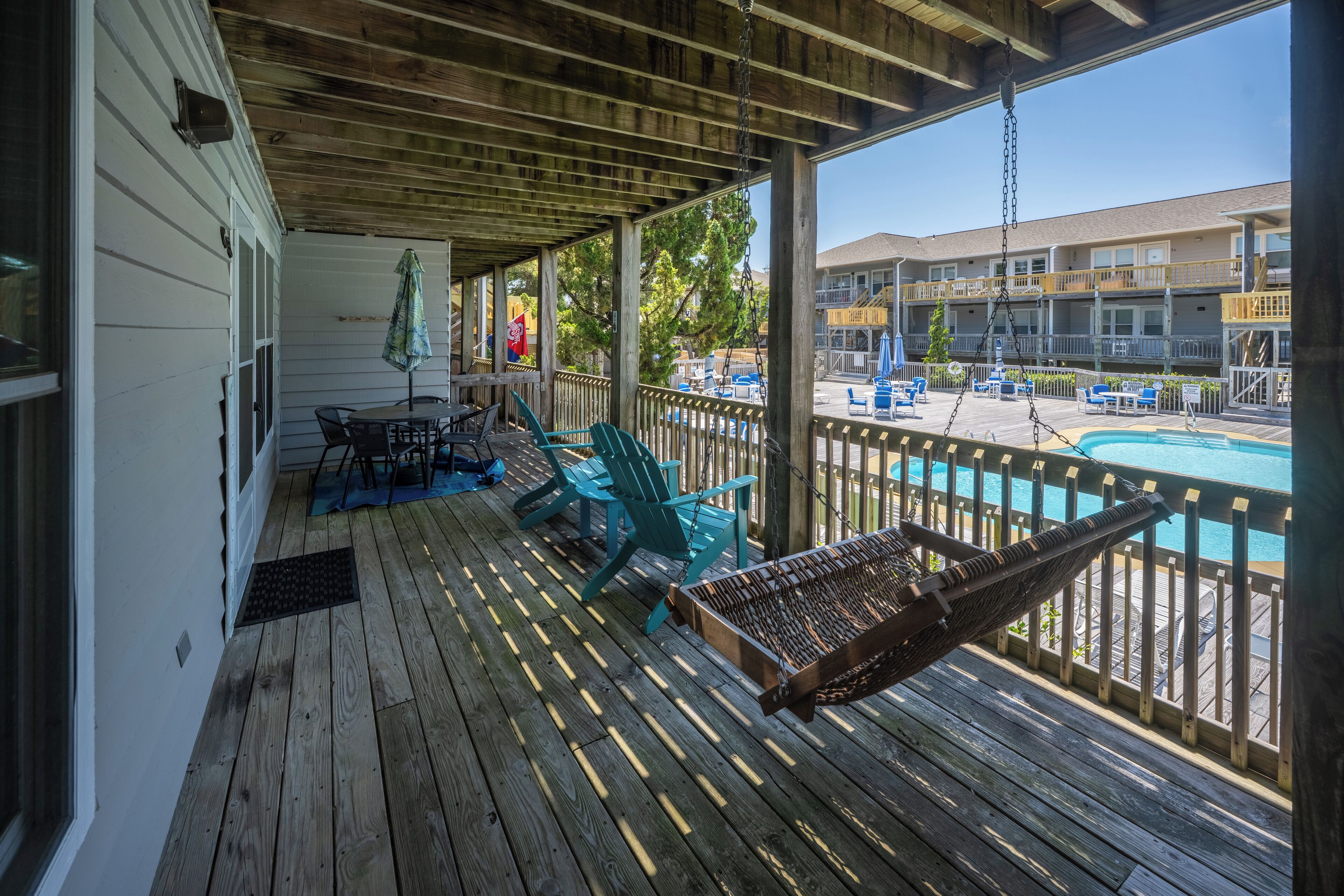 Eine Holzterrasse mit Sitzgelegenheiten im Freien, einem Pool und Blick auf ein Gebäude gegenüber dem Wasser.
