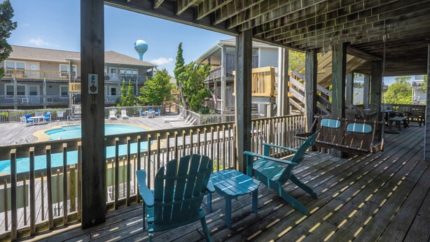 Una terraza de madera con sillas Adirondack y una piscina.