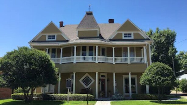 A two-story house with a balcony on the second floor, a front porch, and a chimney. - Kathleen Suite at the Captains House (Granbury)