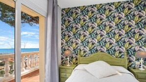 Ein Schlafzimmer mit grünem Kopfteil, einem Bett mit weißer Bettwäsche, einem Nachttisch mit Lampe und einem Balkon mit Meerblick.